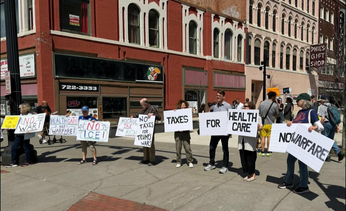 Members line a downtown Binghamton sidewalk holding letter signs reading 'Health care, not warfare'