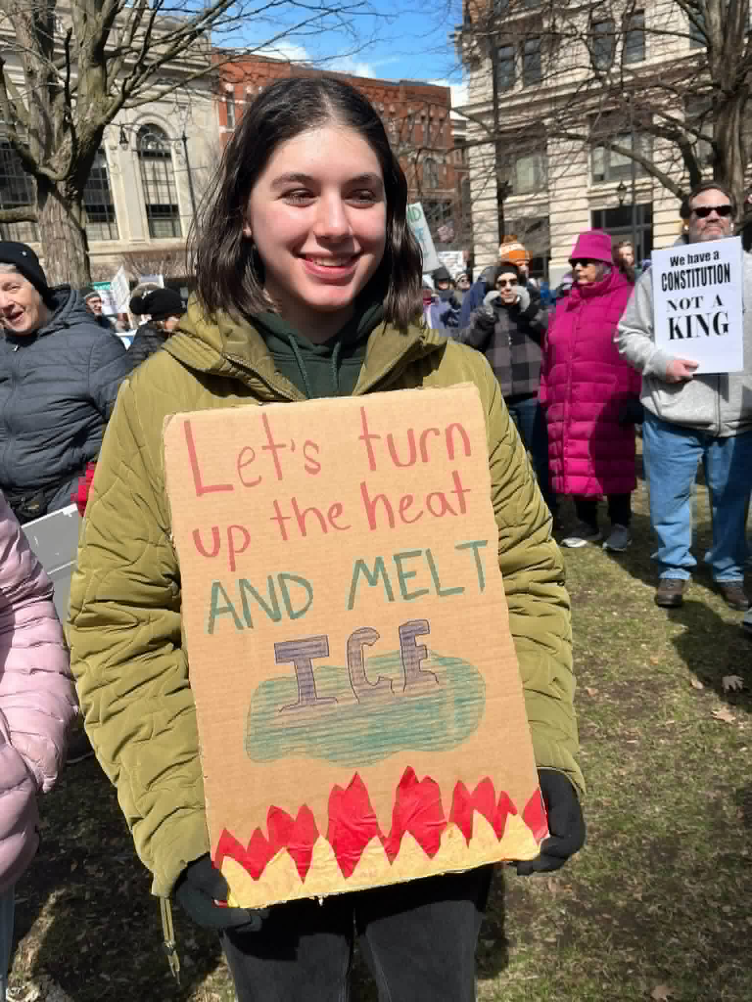 A young protester smiles holding a handmade 'Let's turn up the heat and melt ICE' sign at the No Kings rally